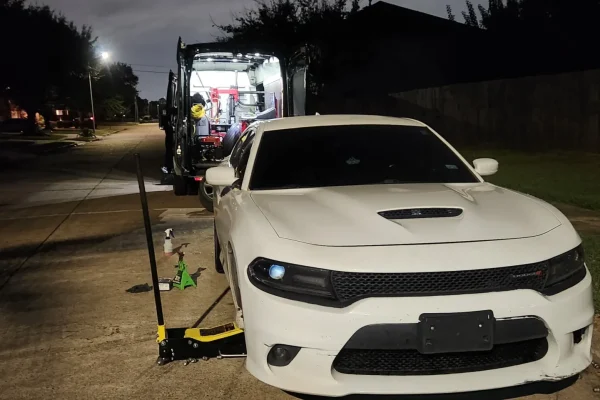 Mobile tire change Houston on Dodge Charger at night with on-site roadside service van and professional jack equipment