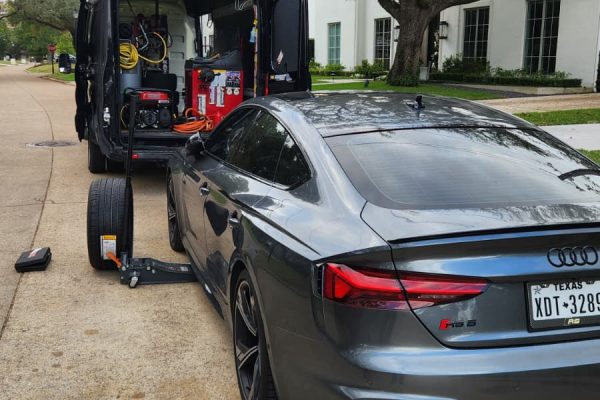 Houston Mobile Tire Service performing on-site tire replacement on an Audi RS5 in a residential neighborhood using a fully equipped mobile tire service van.